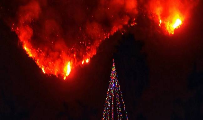 In this photo provided by the Santa Barbara County Fire Department, with flames burning behind it, a Christmas tree stands as a lone sentinel in the front yard of an evacuated home in Carpinteria, Calif., Monday, Dec. 11, 2017. Ash fell like snow and