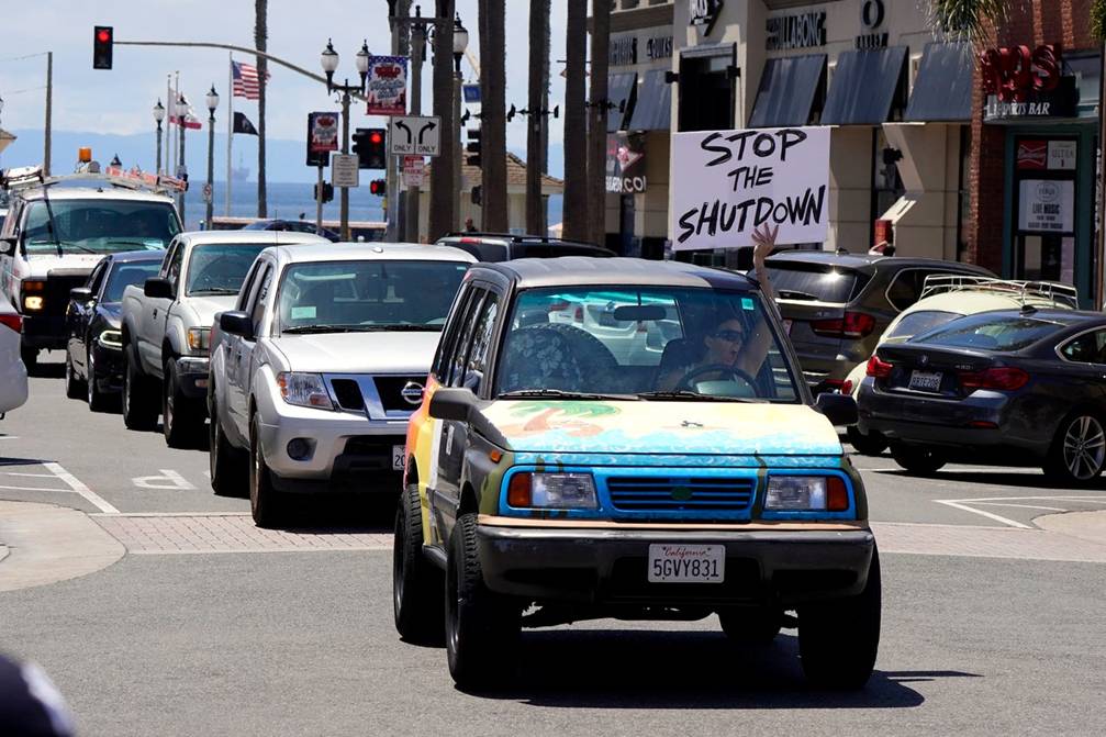 A driver waves a sign at other protesters who were demonstrating against stay-at-home orders that were put in place due to the COVID-19 outbreak, Friday, April 17, 2020, in Huntington Beach, Calif.