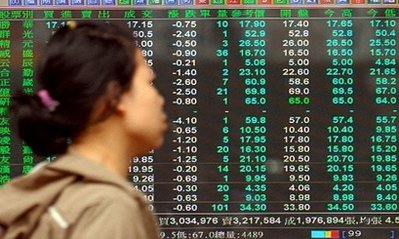 A woman walks past a monitor showing the stocks index figures ...