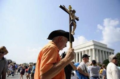 A man carries a crucifix as thousands gather ...